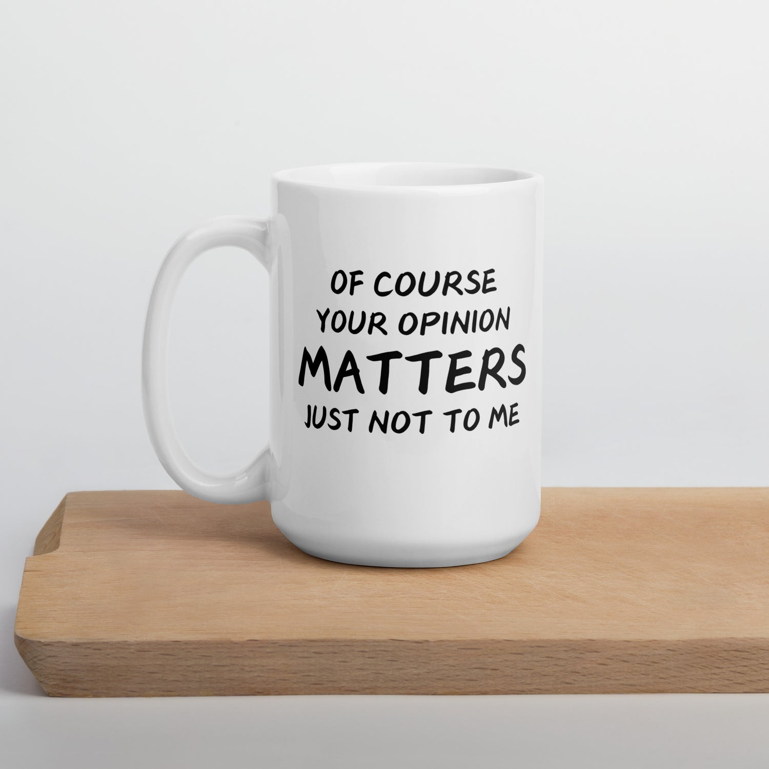 A white ceramic mug with text printed on it, placed on a wooden board, with a humorous quote &